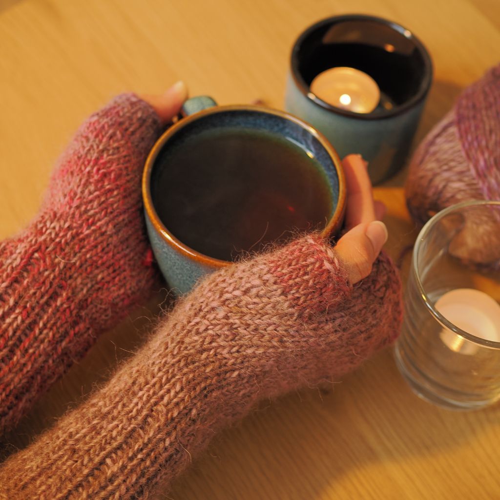 Zwei Hände mit Stulpen die eine heiße Tasse Tee festhalten.