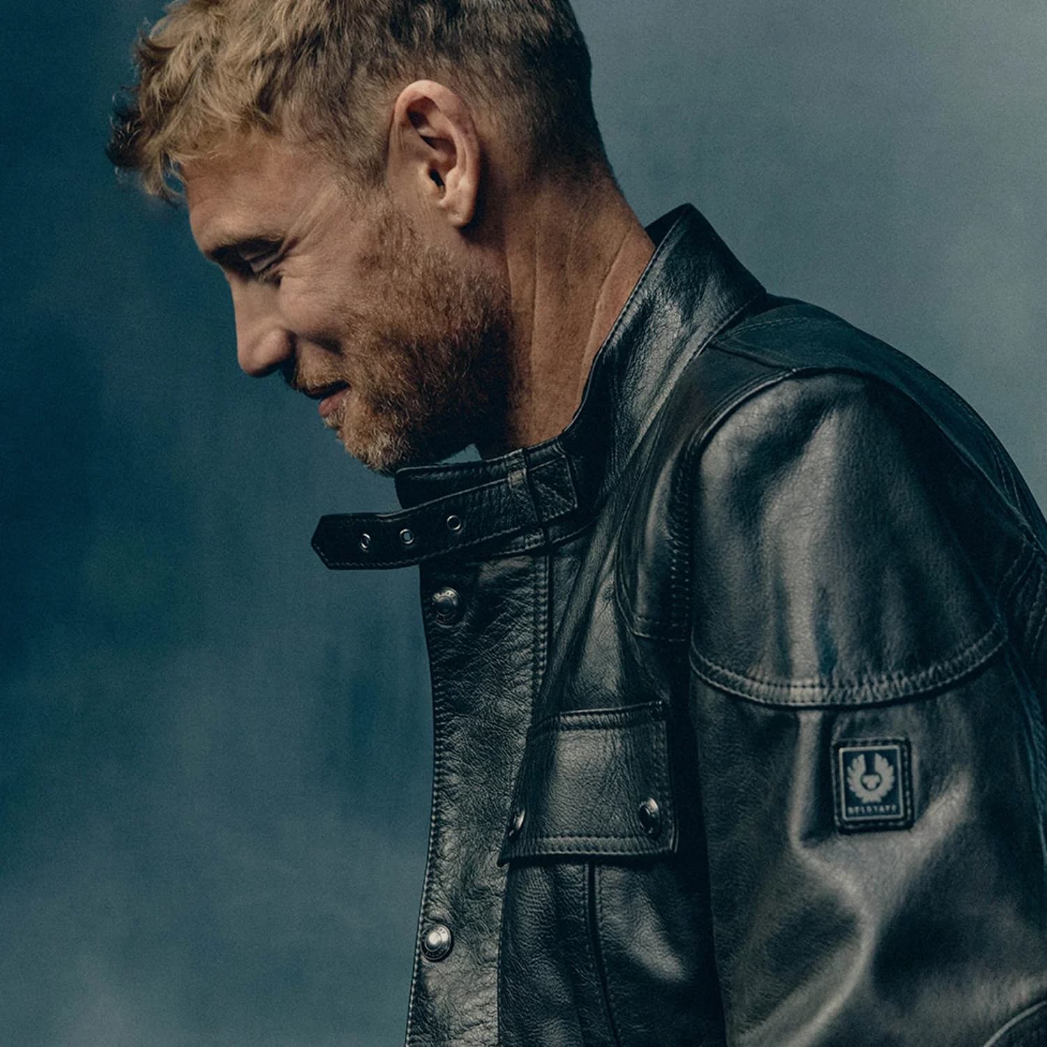 Man in a black leather jacket looking down thoughtfully.