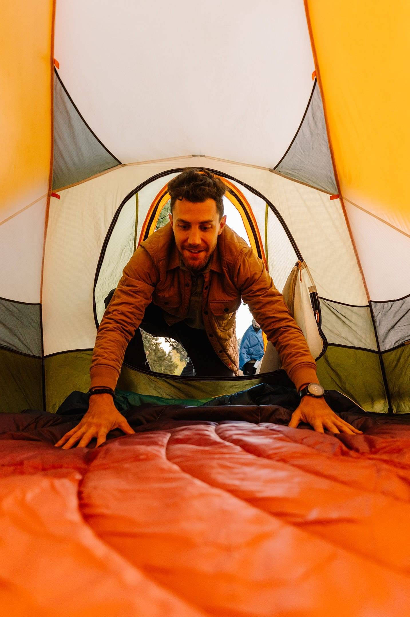 Man laying down a camping blanket inside his tent