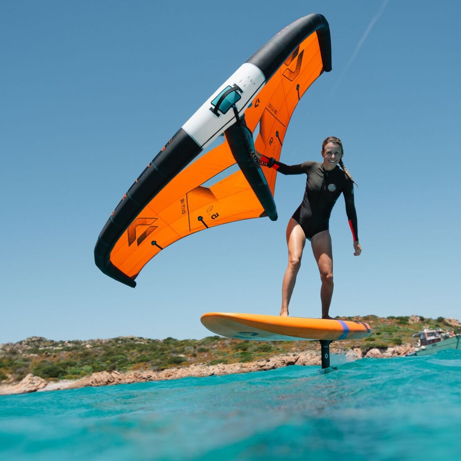 Person surfing on water with a winged foil board against a clear sky.