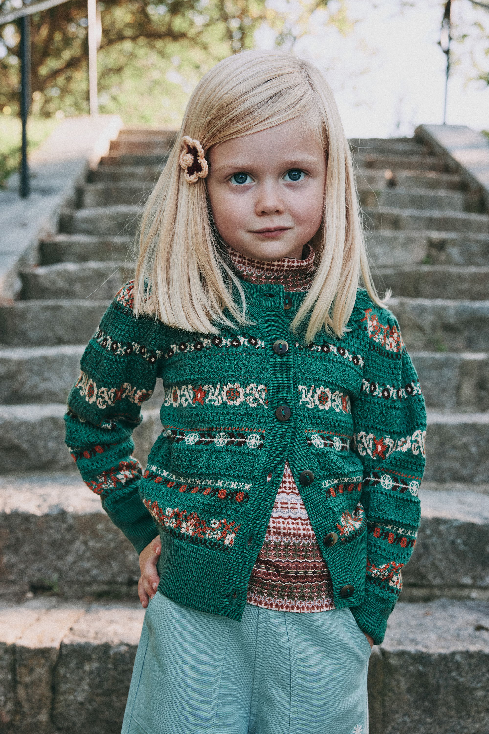Child in a green patterned sweater, standing on stone steps.