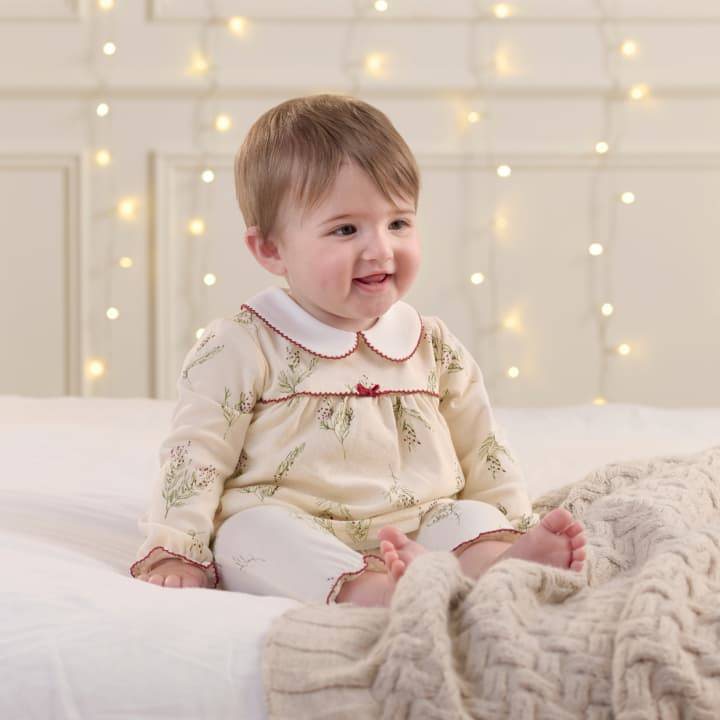 Smiling baby girl sitting on bed wearing pyjamas