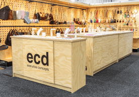 Wooden display counters with handbags and accessories in a retail setting.