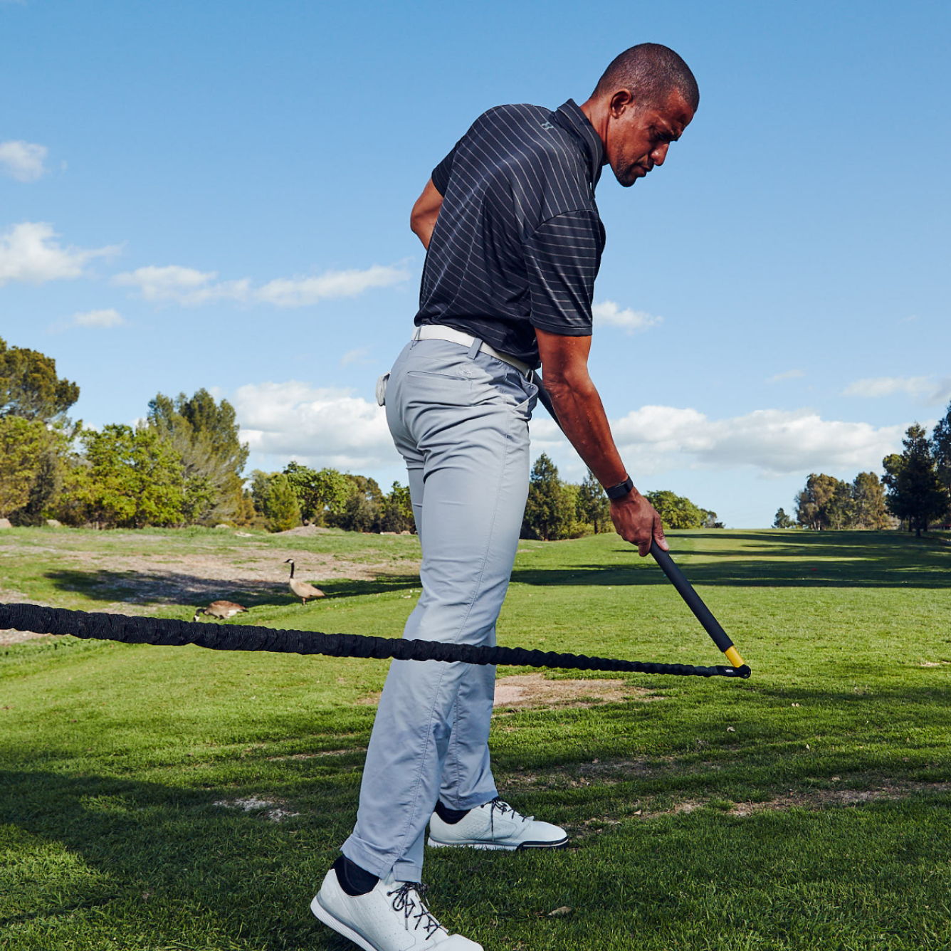 A golfer practicing a swing with a TRX Rip Trainer on a sunny day.