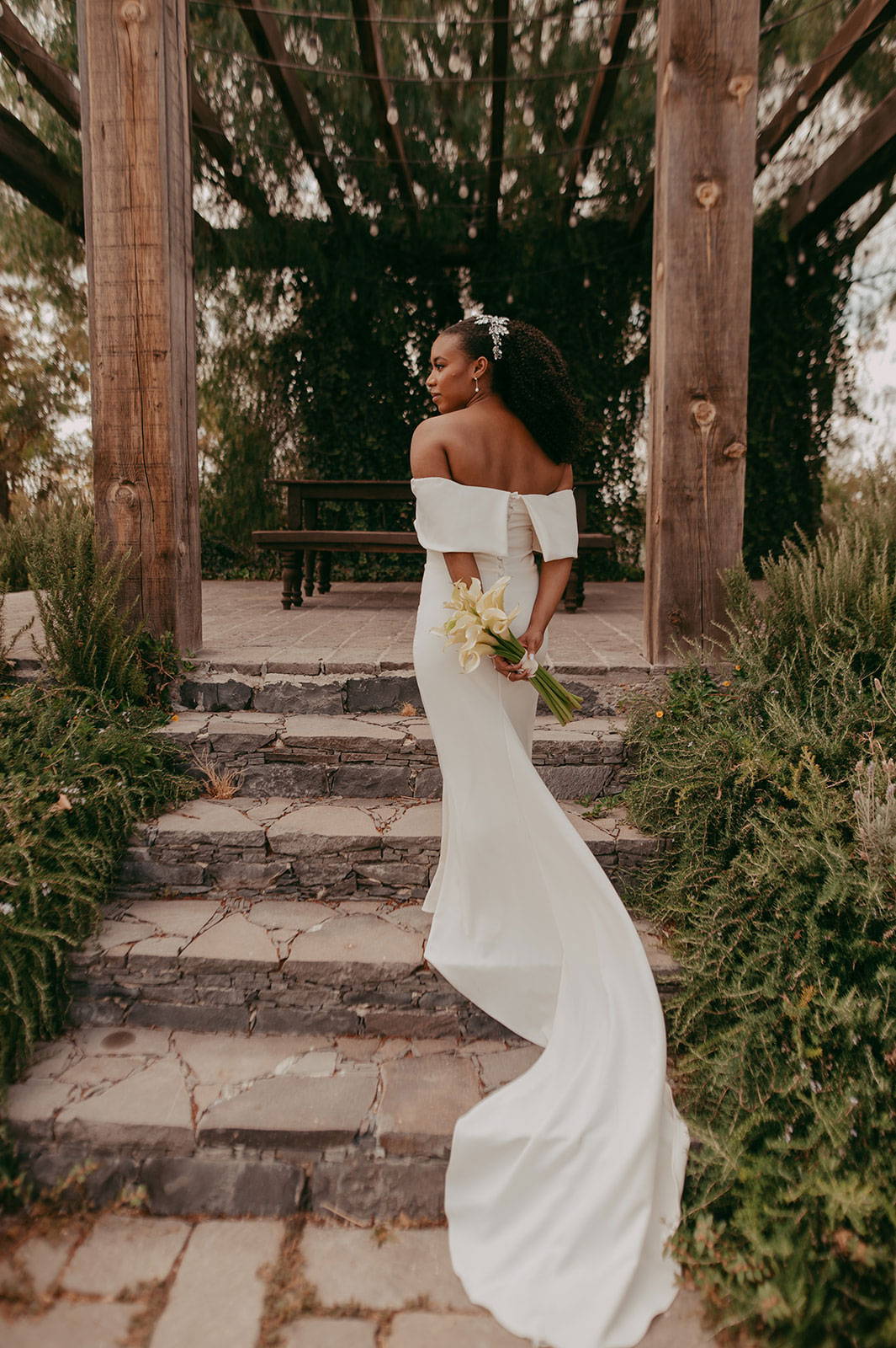 Bride on steps wearing the Mila Gown and holding a bouquet