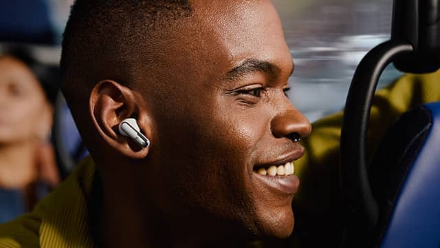 Smiling person wearing wireless earbuds on public transportation.