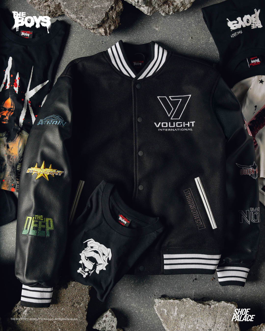 Shoe Palace x The Boys - Black varsity jacket surrounded by graphic t-shirts on a textured surface.
