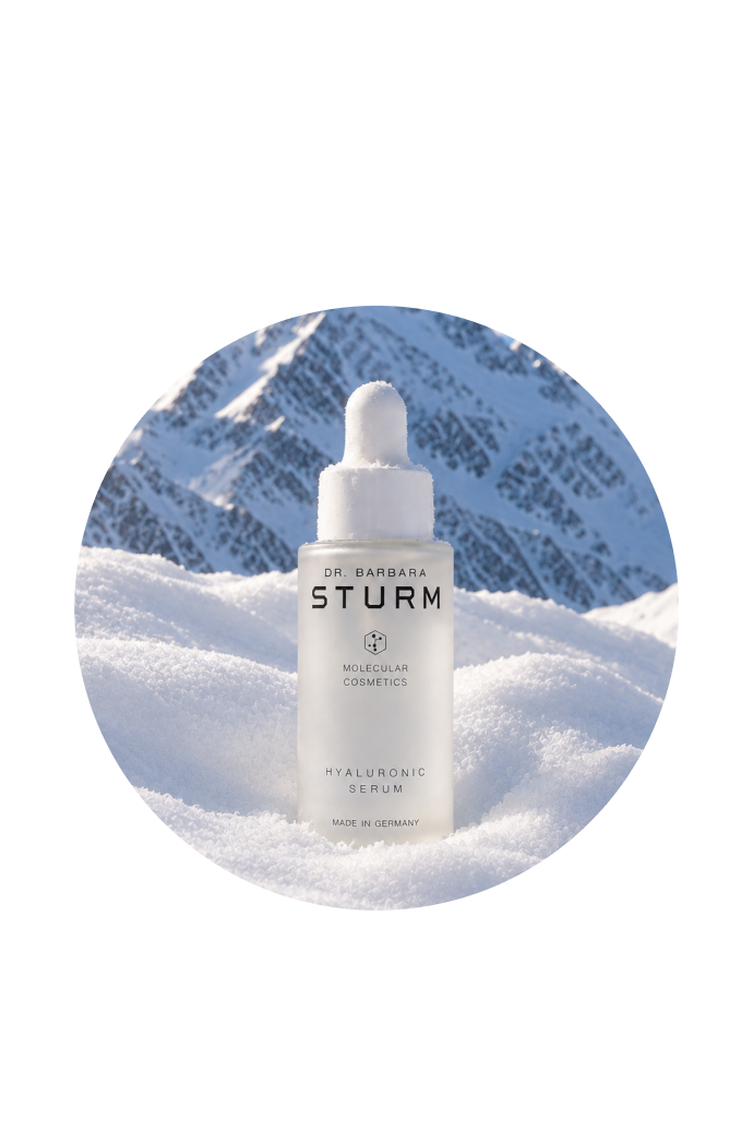 Bottle of skincare serum on snow, with mountains in the background.