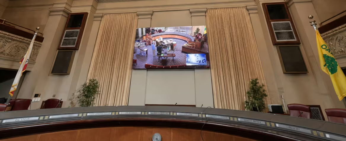 Interior of a legislative chamber with a large screen and flags.