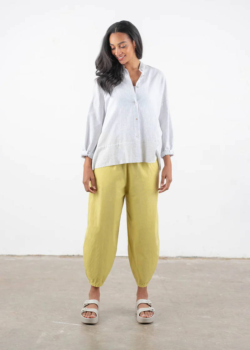 A model wearing a white boxy long sleeved shirt with yellow barrel legged cotton trousers and off white chunky platform slides