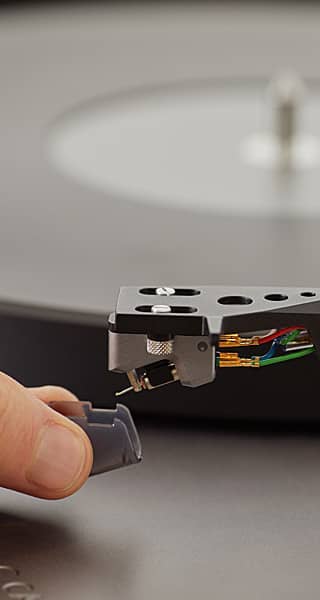 A hand attaching a cartridge to a turntable's tonearm.