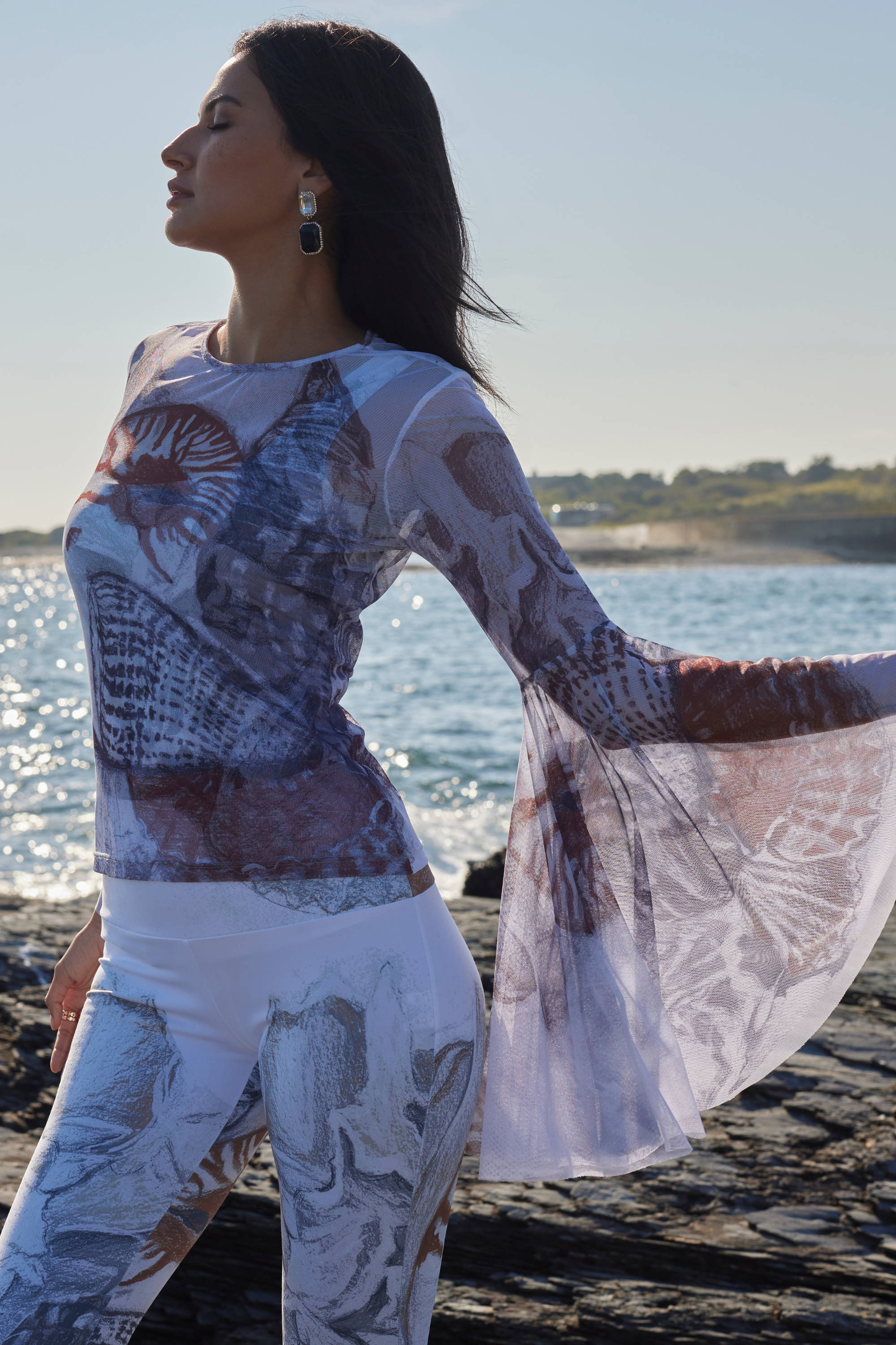 Woman wearing mesh printed top with fun sleeves and matching pants by the water by Ala von Auersperg