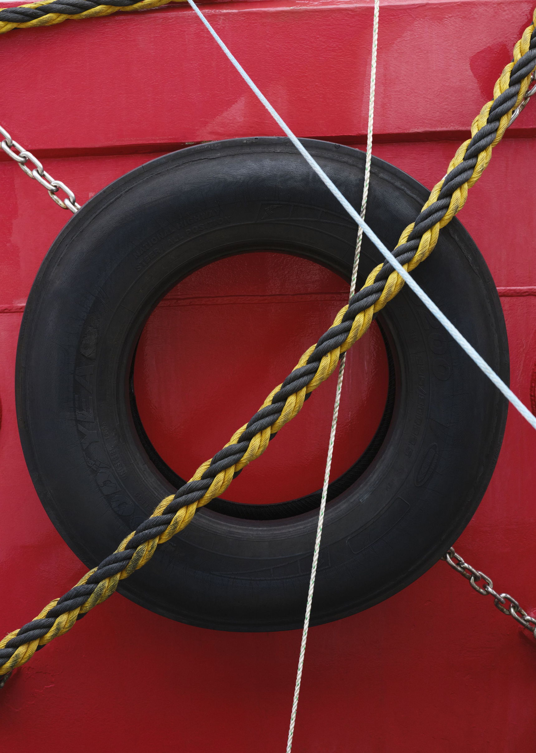 A black tire hanging against a red background with braided ropes.