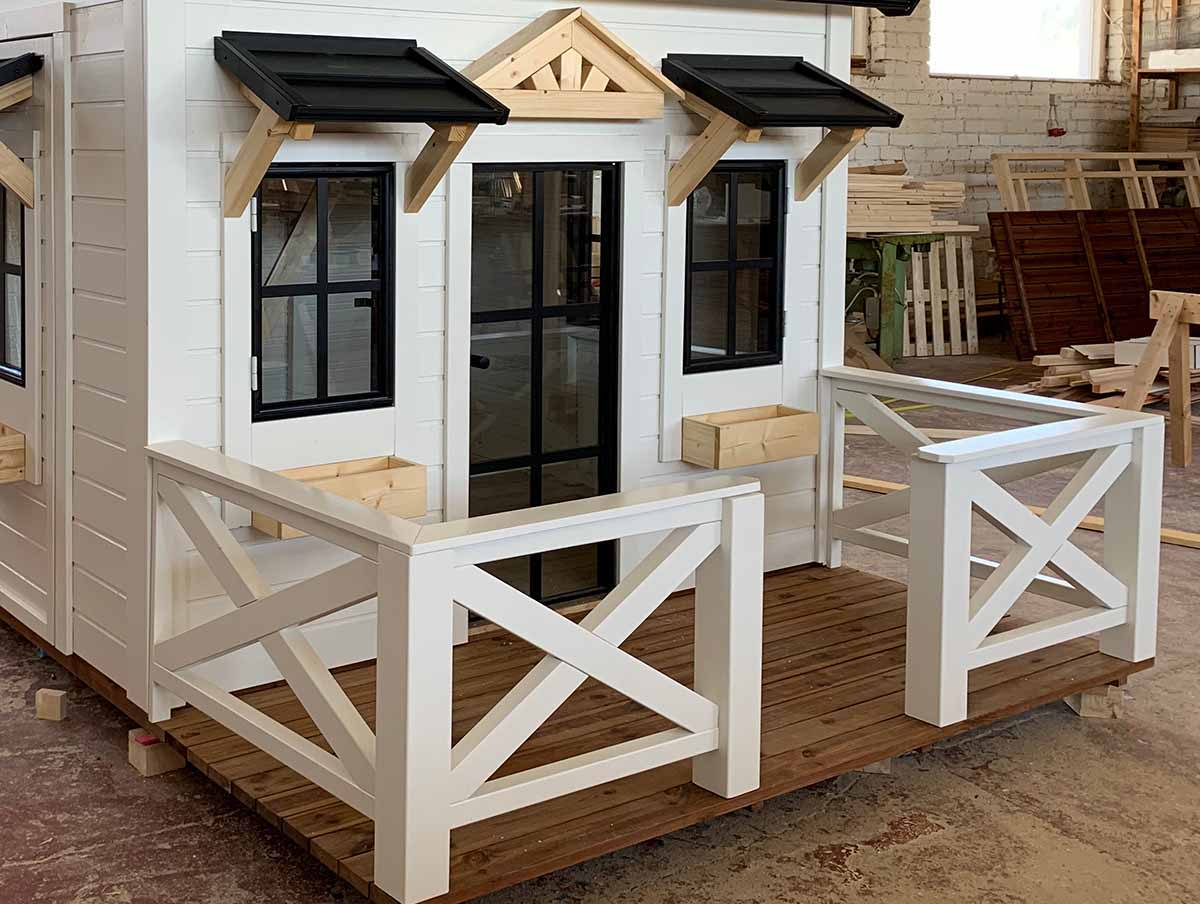 Custom Outdoor Playhouse from Front with wooden terrace with white railings and glass door by WholeWoodPlayhouses 