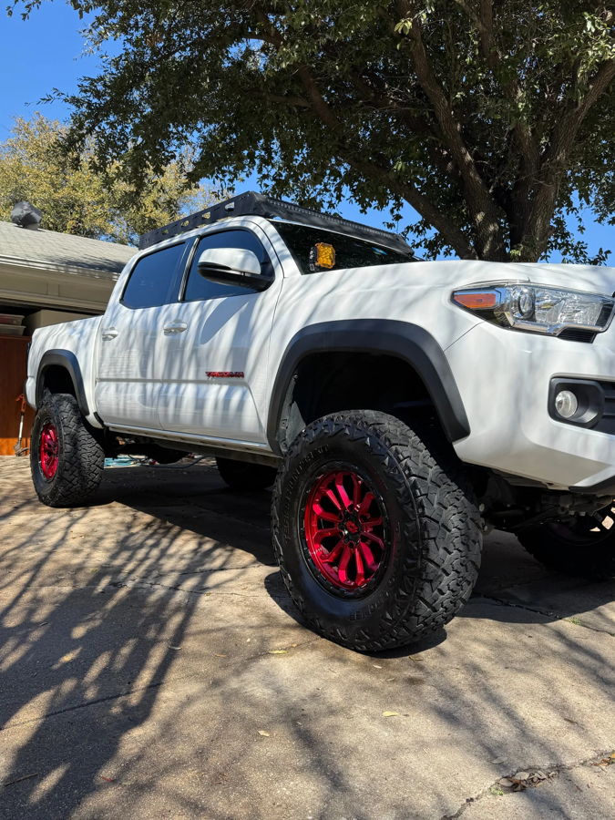 Low-angle white Tacoma red metallic wheels Terra Hunter tires tree shadows blue sky Joel's 2021 Tacoma 2-Chime 3-Liter gallery photo 3