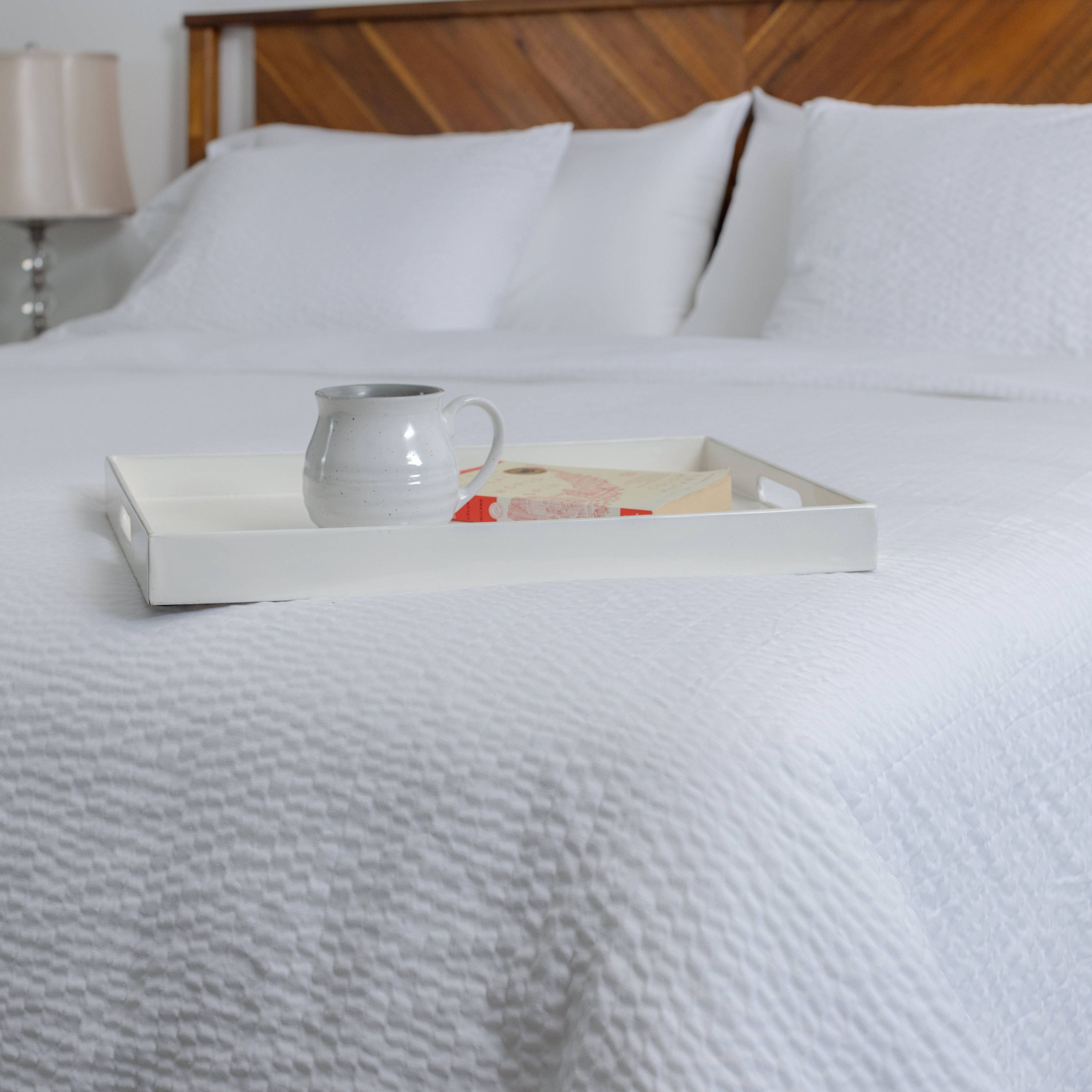 A bed made up with textured white sheets and a tray of coffee and treats set upon it