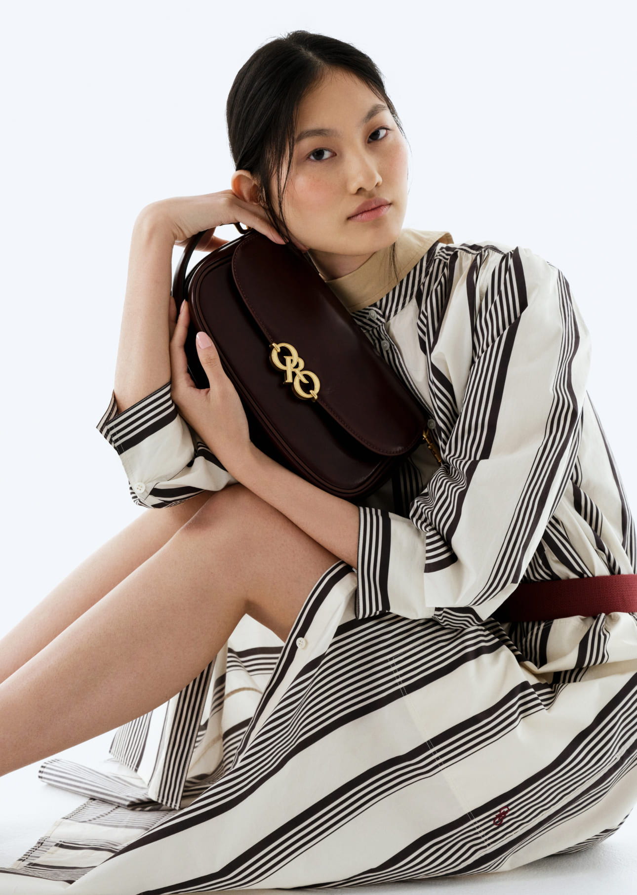 A model wearing a striped dress holding a burgundy handbag.