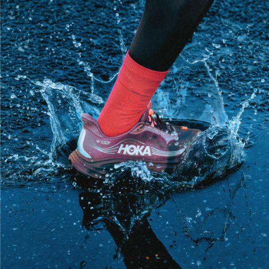 A foot in HOKA shoes splashing through water.