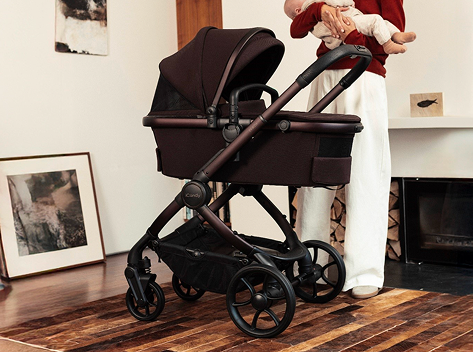 Person holding a baby next to a stroller in a cozy room.