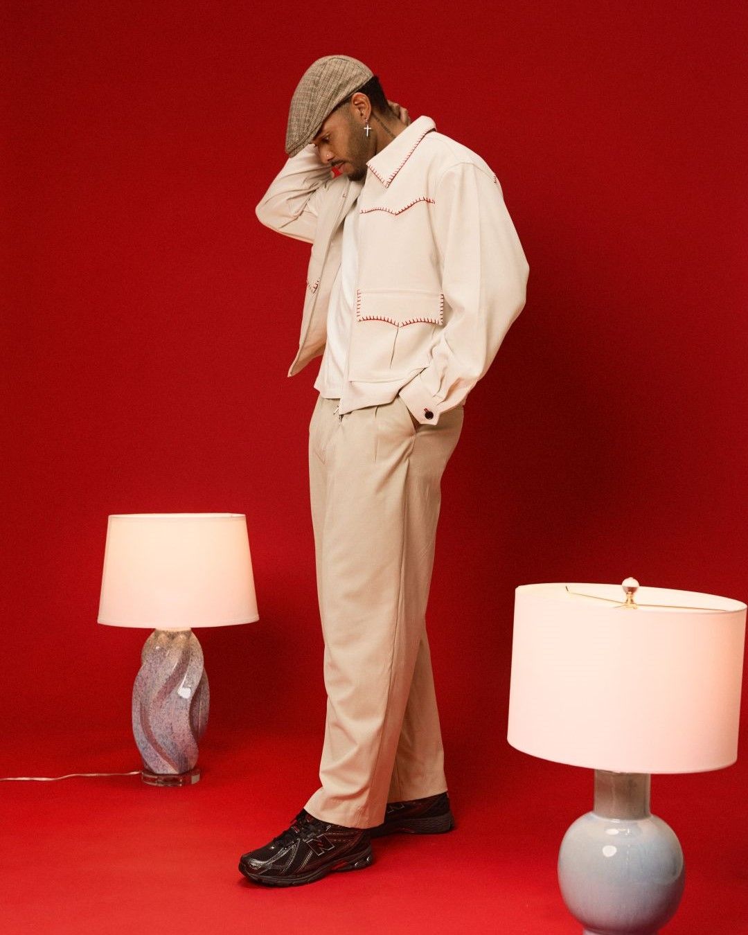 Person in stylish outfit standing between two lamps against a red background.