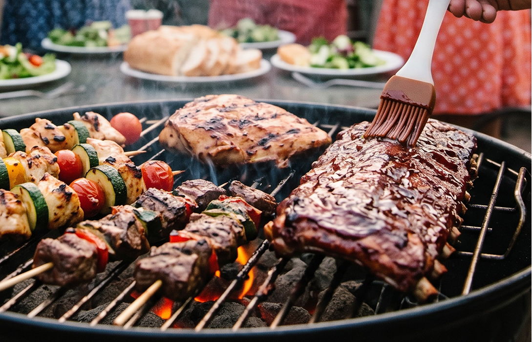 ribs and veggies on a grill being brushed with a grill sauce