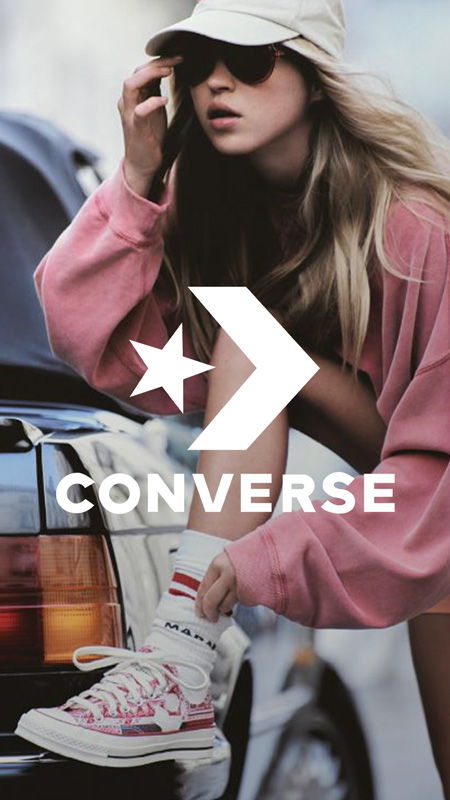 Woman in casual attire posing with Converse shoes near a car.