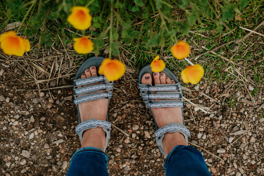 woman standing with sandals next to flowers