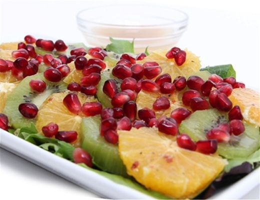 A vibrant fruit salad with oranges, kiwis, pomegranates, and dressing.