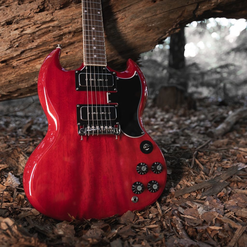 Red electric guitar resting on the ground near a tree.
