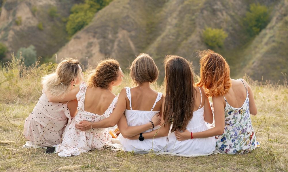 Five women sitting together, facing a scenic landscape, embracing friendship.