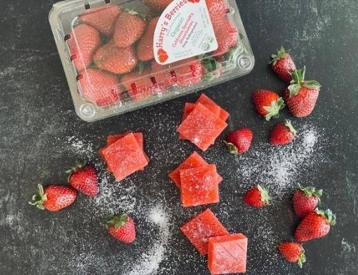 Fresh strawberries and red candy pieces on a dark surface with powdered sugar.