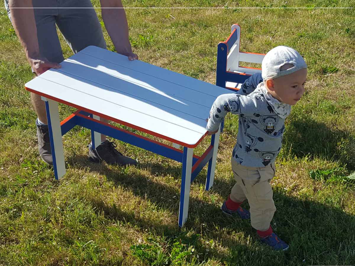 A boy helps to move the kids table to the playhouse by WholeWoodPlayhouses