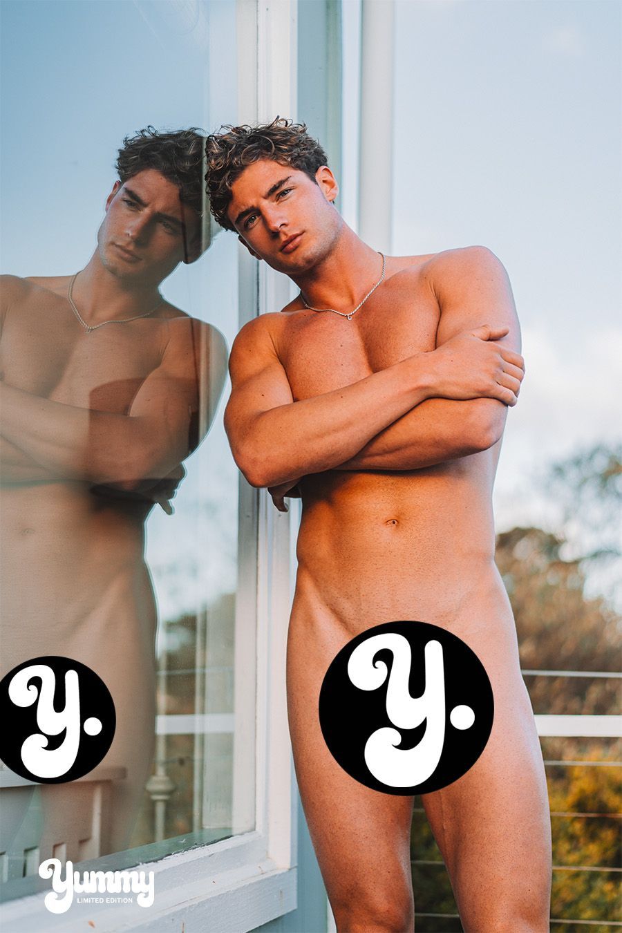 Young man posing nude in front of a window, with logos obscuring private areas.