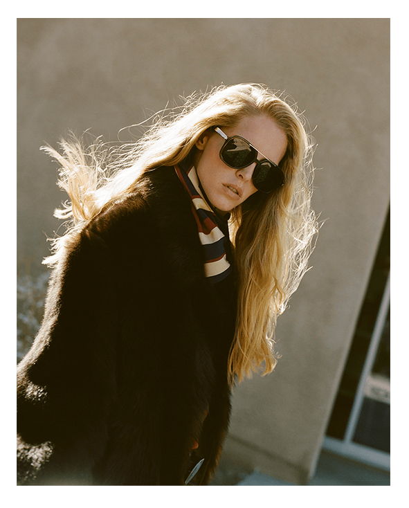 A woman with long hair wearing sunglasses and a scarf.