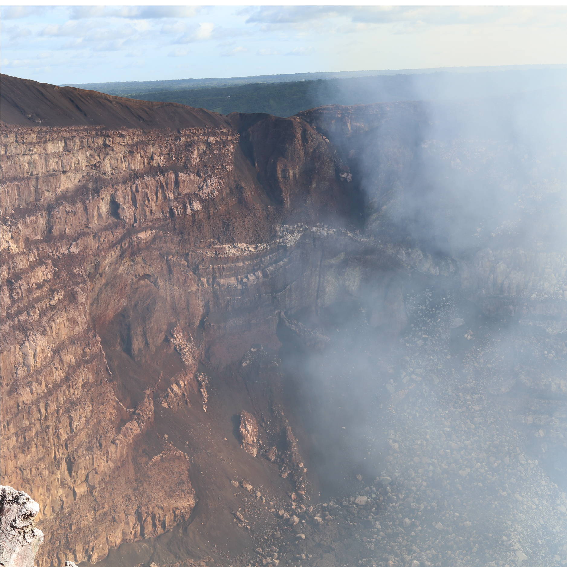 The steep edge of a volcano in Nicaragua. Large Rocks can be seen below as smoke rises from the center.  