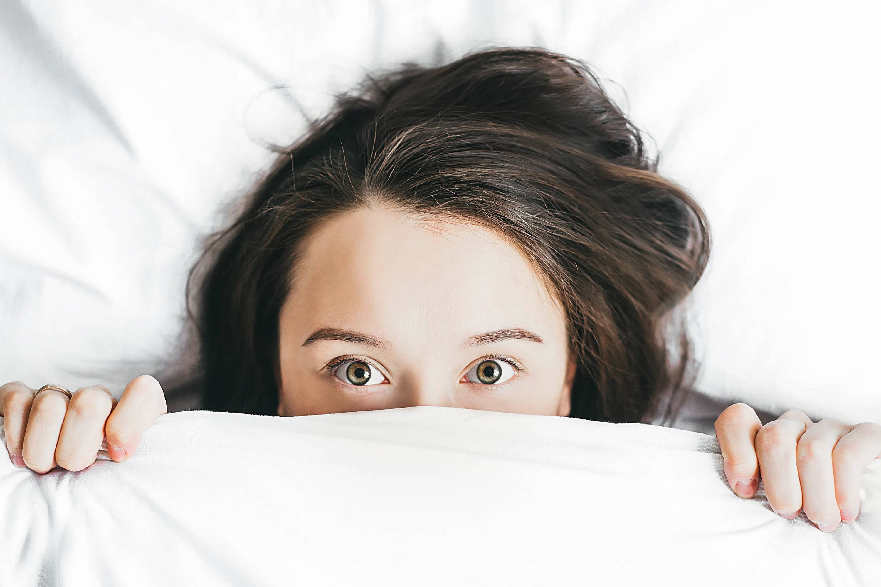 woman peaking out from under bed covers