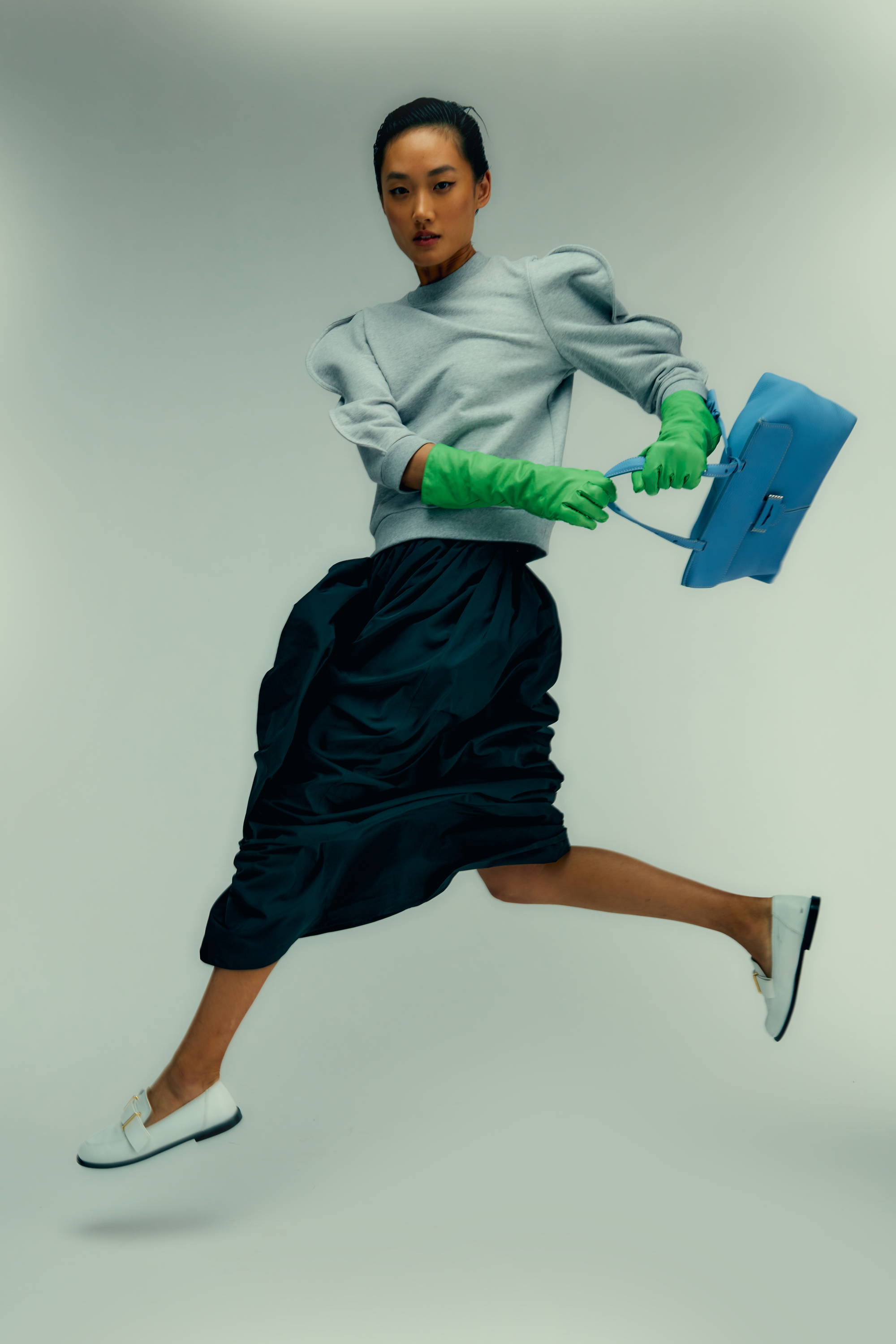 Woman in stylish outfit jumping with a blue bag and green gloves.