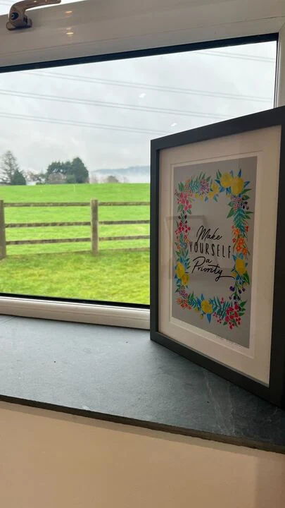 Framed artwork on a windowsill with a green field outside.