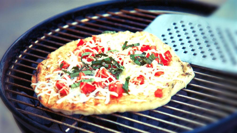 pizza on a grill with tomatoes and basil and cheese