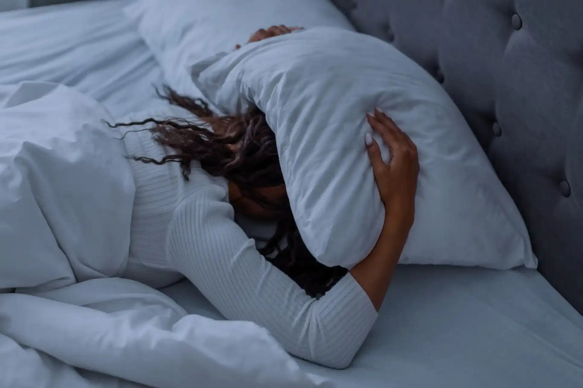 Vrouw ligt op haar buik in bed met een kussen over haar hoofd; het is donker maar ze kan niet slapen door huisstofmijtallergie. Haar neus zit verstopt, ze heeft overal jeuk en moet steeds niezen en snuiten.