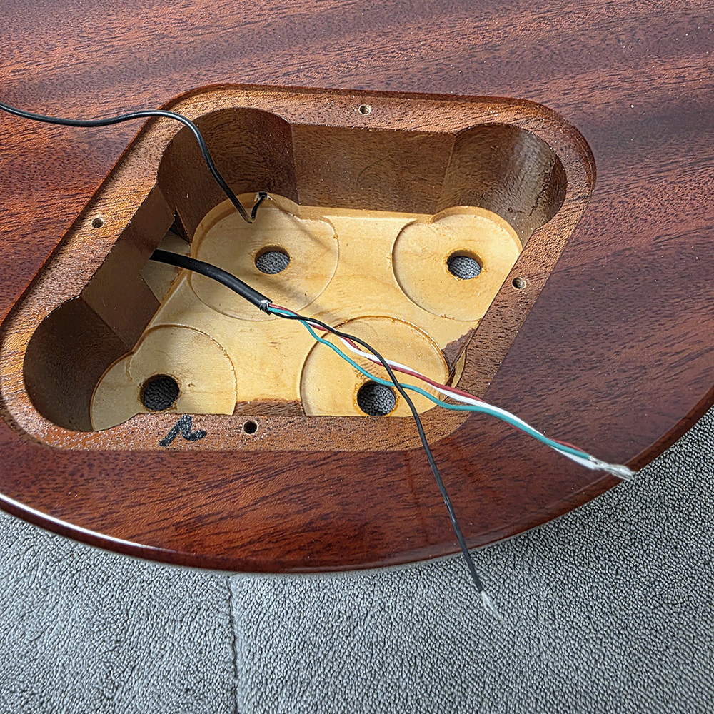 Electrical wiring inside a wooden guitar body cavity.