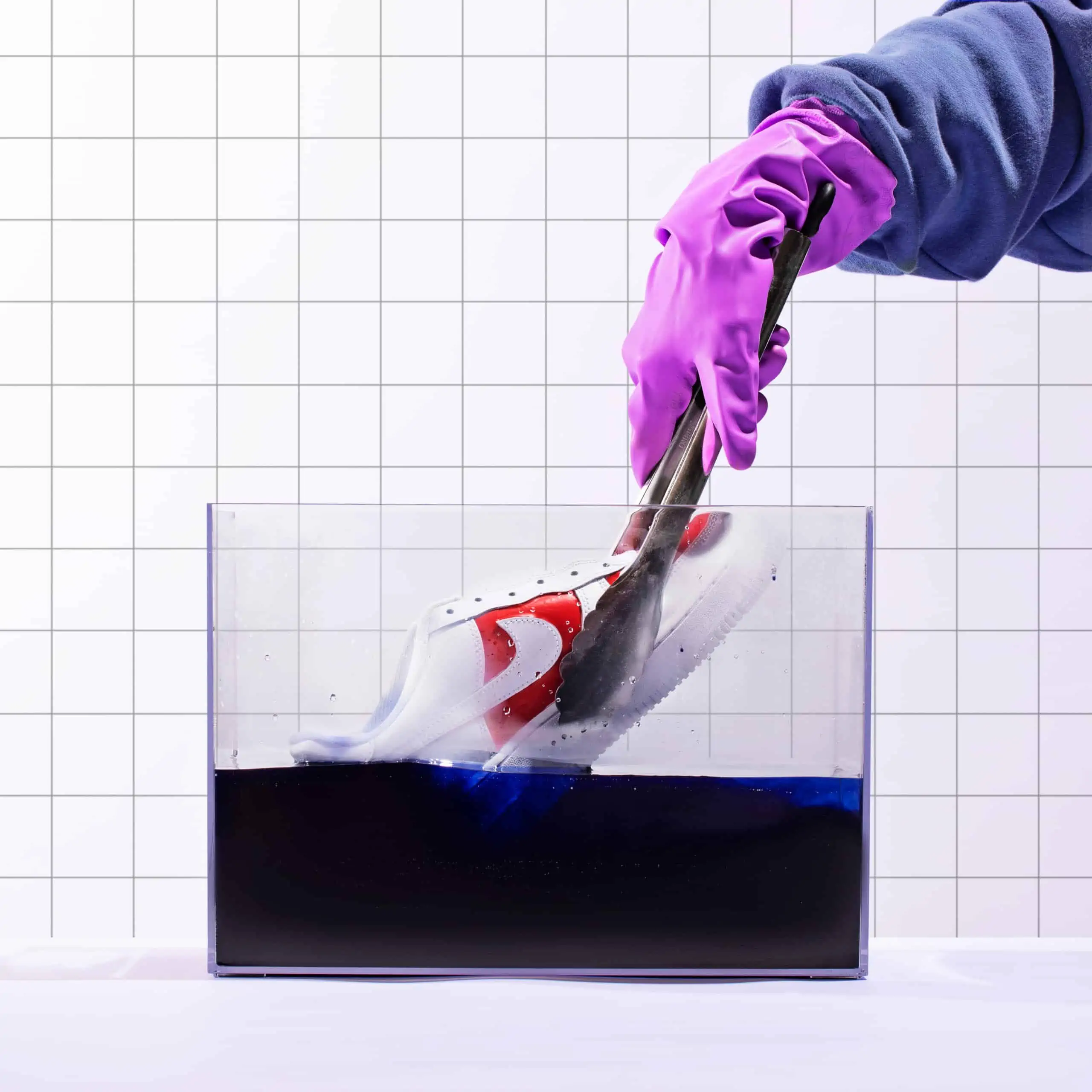 A gloved hand dipping a shoe into blue dye in a container.
