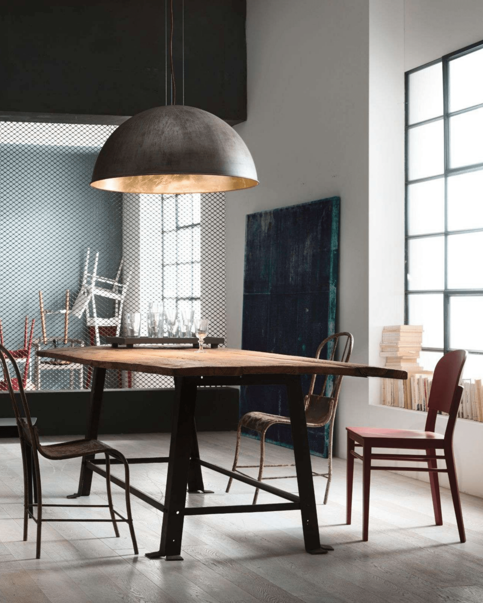 Dining area with a wooden table, brass dome pendant and chairs in a modern interior setting. 