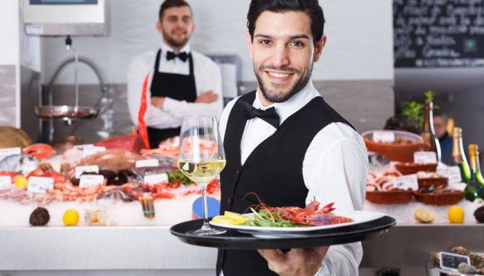 Caterer wearing black bow tie and vest with food display