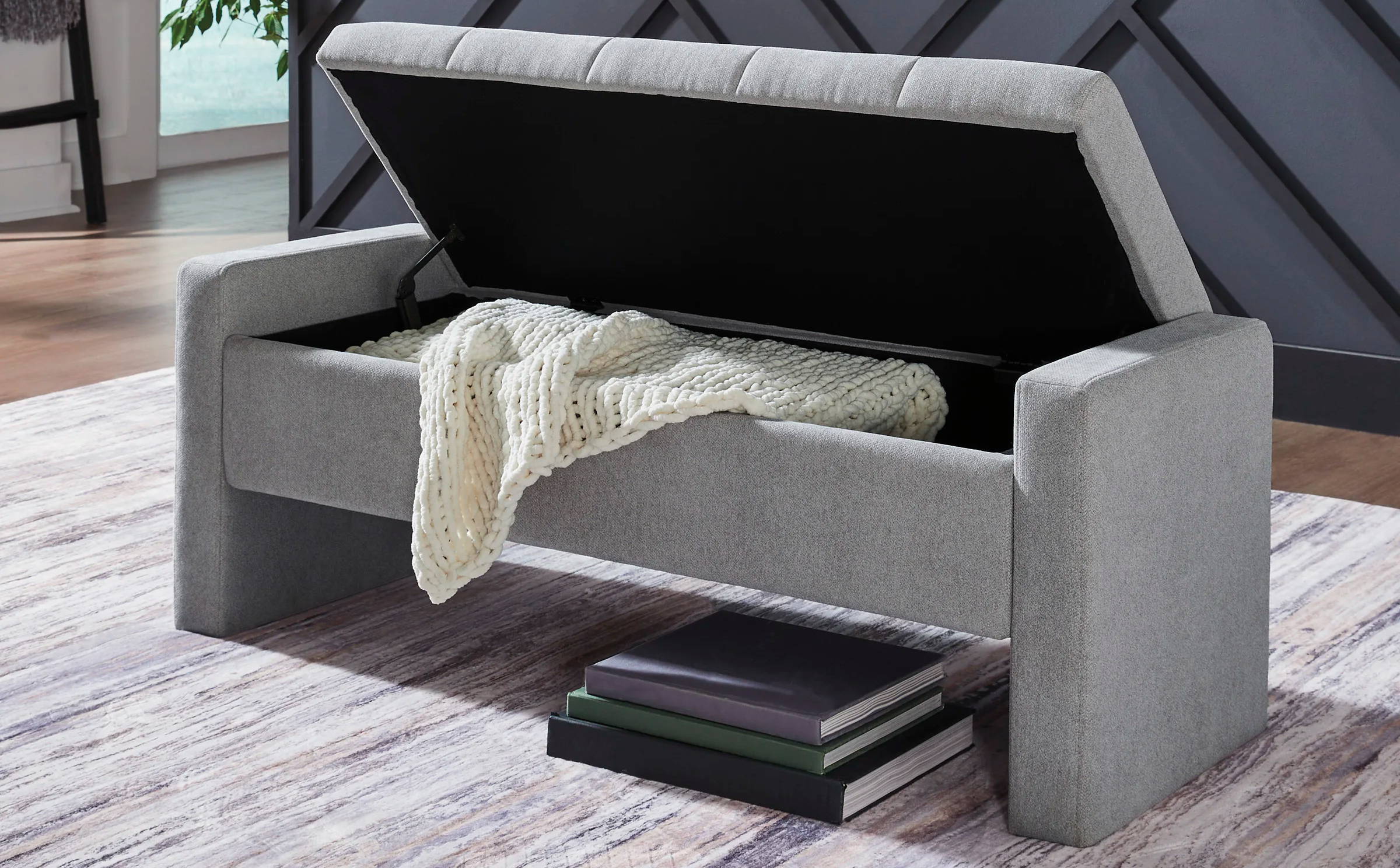 Gray storage bench with an open lid, placed on a patterned rug.