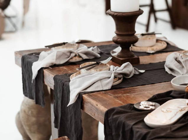 Platos y cuencos sobre mesa de madera con servilletas grises y caminos de mesa negros