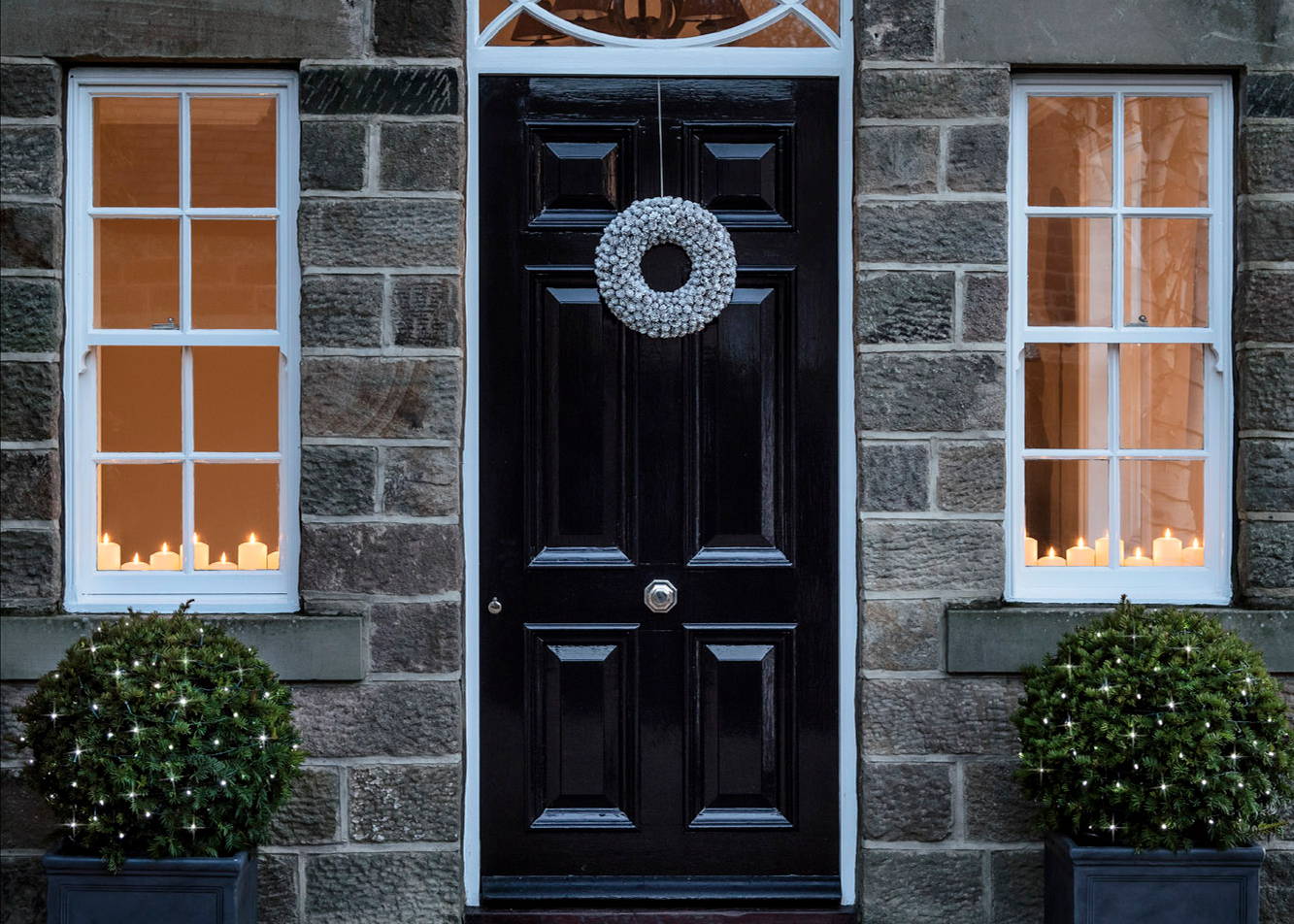 A front door with a wreath and two small shrubs placed either side