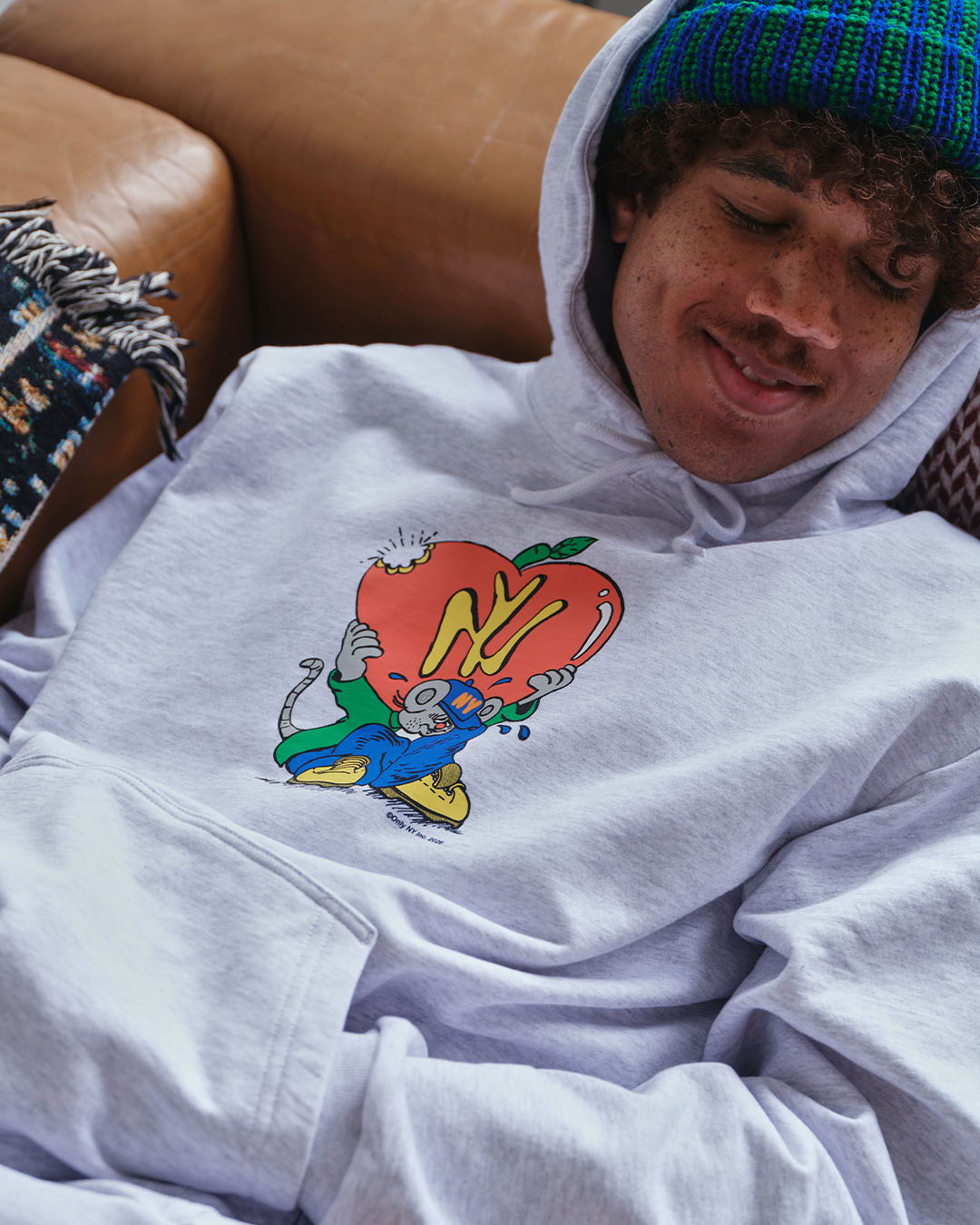 Person wearing a hoodie with an animated character design, relaxing on a couch.