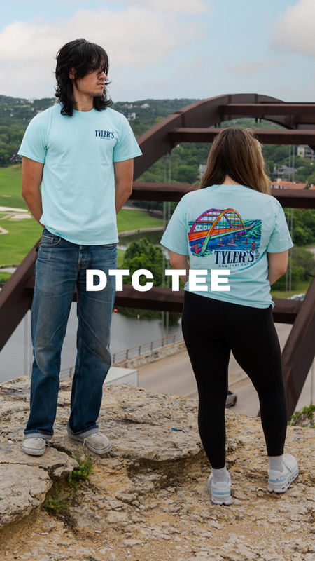 Two people wearing matching light blue T-shirts outdoors near a bridge.