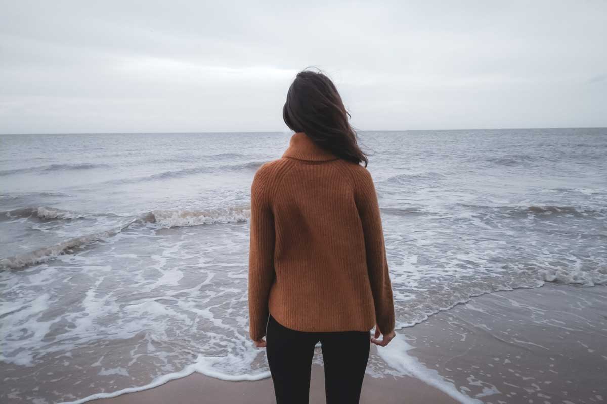 A woman on the edge a body of water, dressed in a sweater and pants